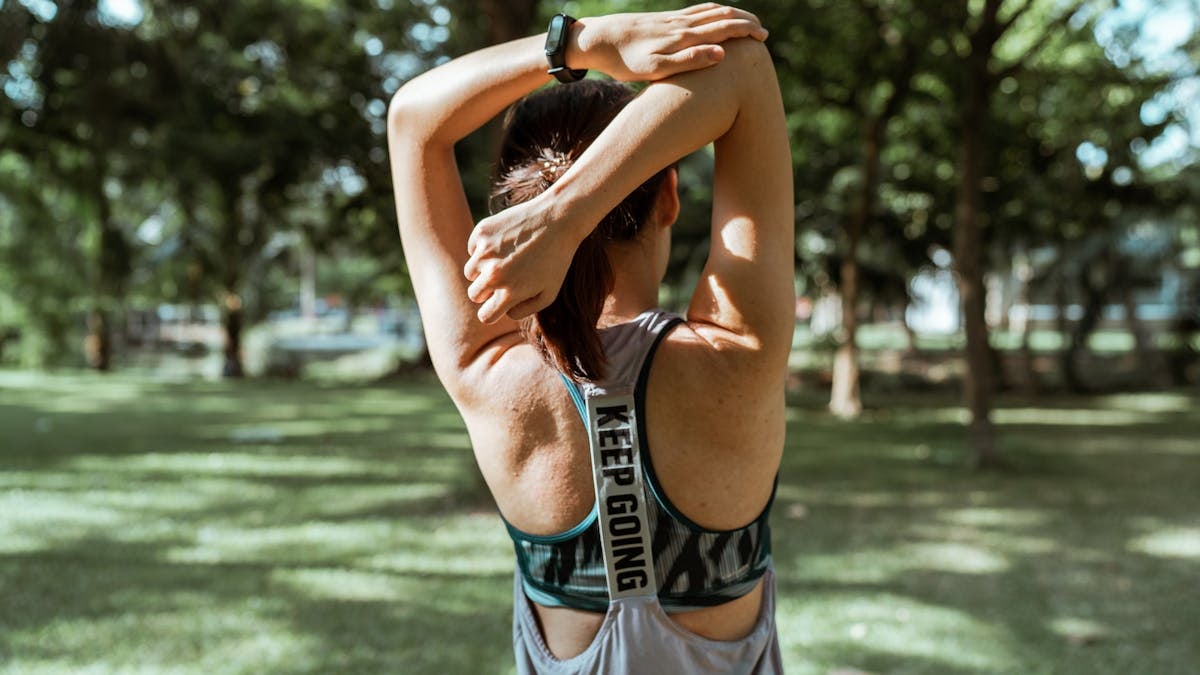 Back view of anonymous sportswoman in activewear doing stretching exercise for back and arms alone in park